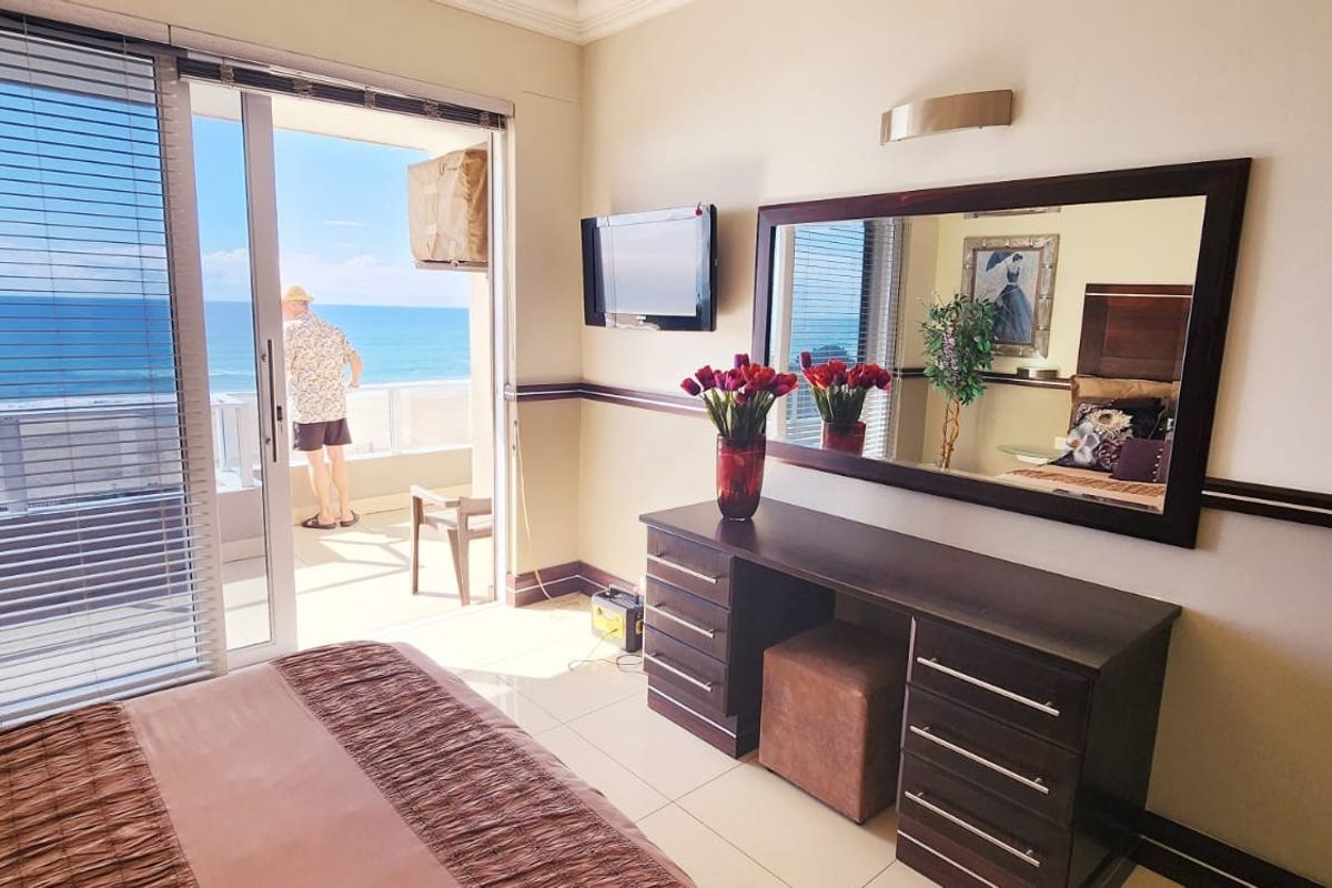 A bedroom featuring tiled flooring, a wall-mounted vanity mirror, and sliding glass doors opening onto a balcony with ocean views.