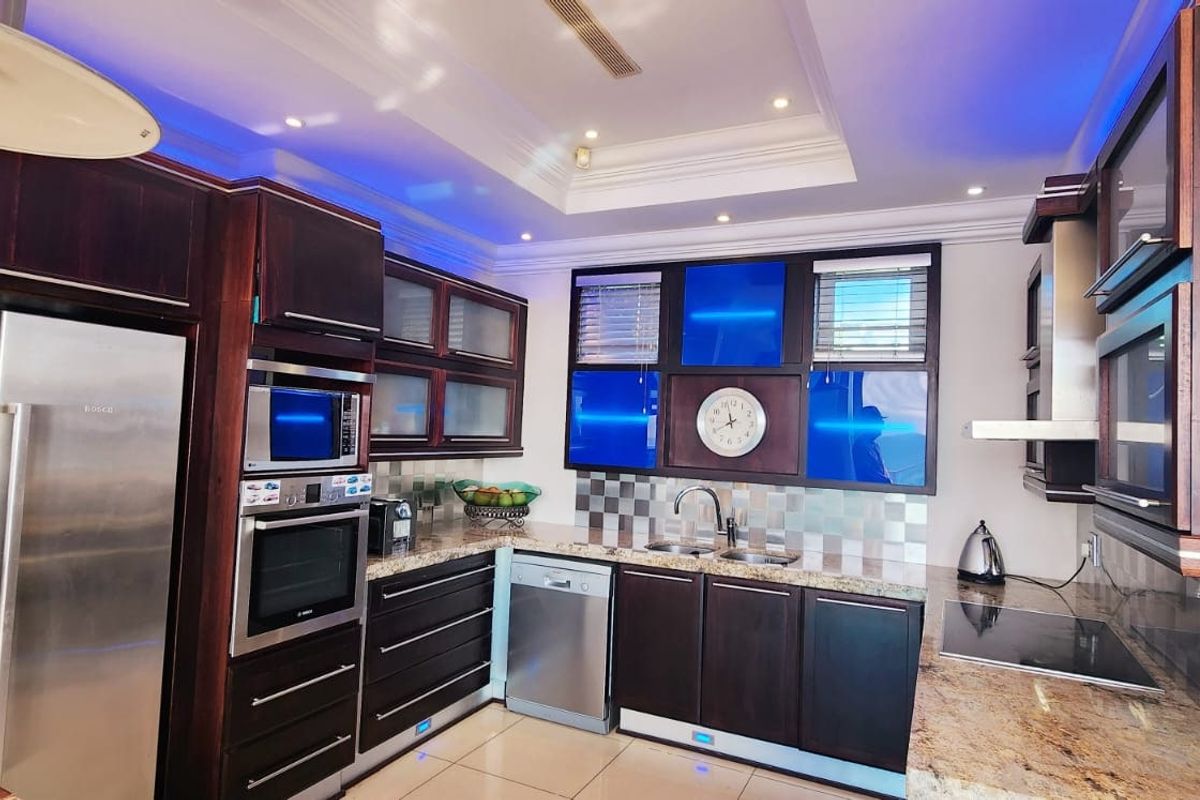 Modern kitchen featuring dark wood cabinetry, granite countertops, integrated stainless steel appliances, and decorative blue accent lighting with a tray ceiling.