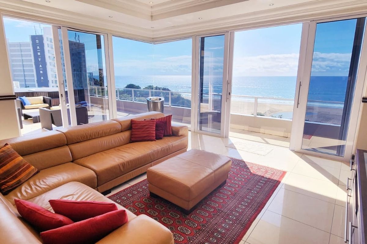 Spacious living area featuring large glass sliding doors that open onto a balcony with panoramic ocean views and modern tiled flooring.