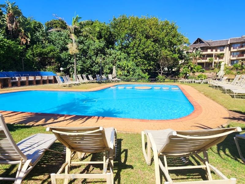 Communal swimming pool area featuring a paved surround, landscaped garden setting, and adjacent apartment complex buildings.