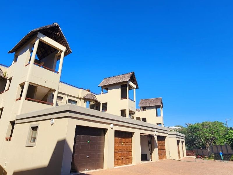 Exterior view of a multi-story apartment complex featuring thatched roof accents, multiple garage doors, and paved driveway access.
