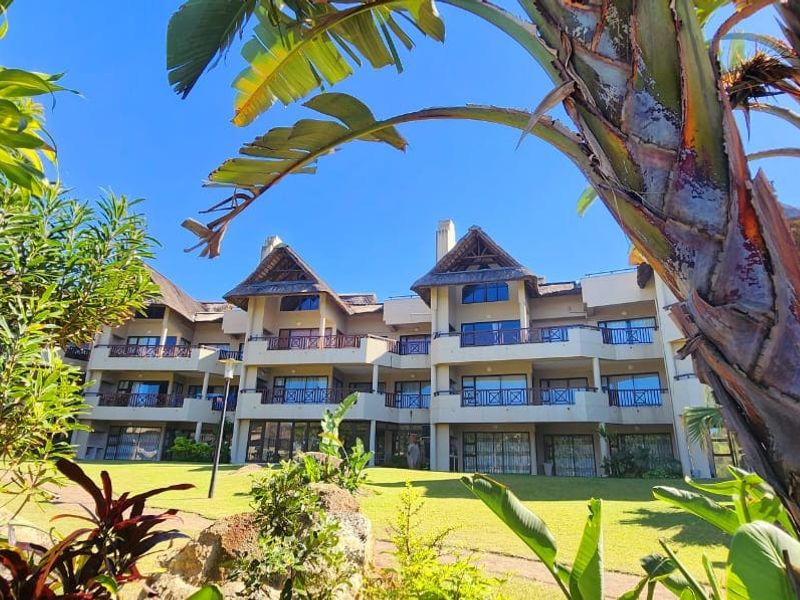 View of the apartment complex exterior featuring multi-level balconies, thatched roof detailing, and landscaped garden surroundings.