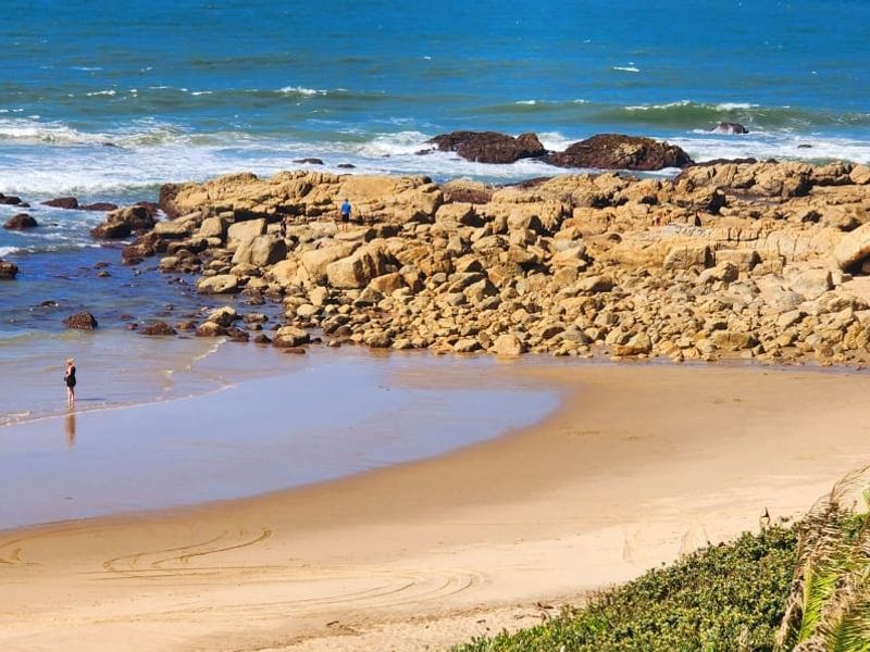 A scenic coastal view featuring a sandy beach, rocky shoreline, and the ocean, highlighting the property's proximity to natural coastal landscapes.