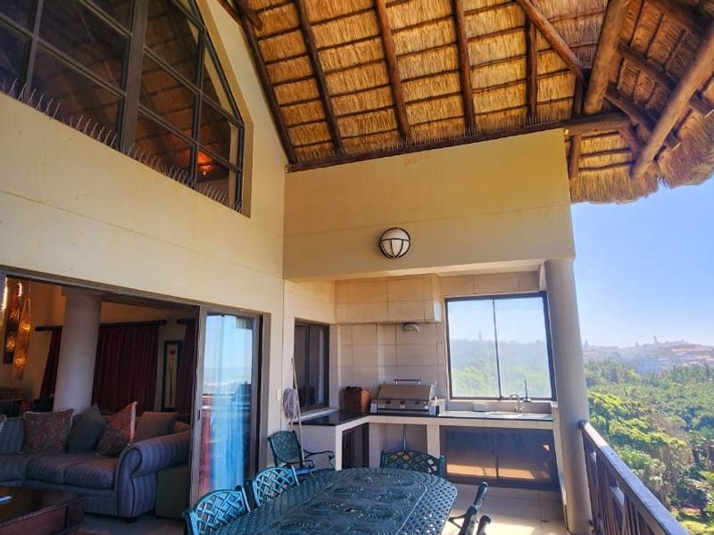 Spacious covered balcony featuring a built-in braai area, high thatched ceiling, and expansive coastal views, seamlessly connecting to the interior living space.