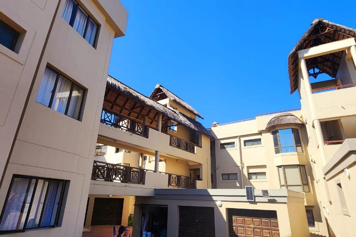 Exterior view of a multi-story apartment complex featuring thatched roof accents, balconies with wooden railings, and integrated garage doors.