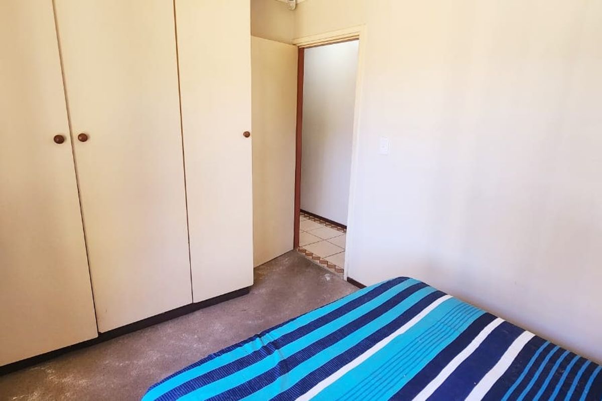 A bedroom featuring built-in cupboards and direct access to an adjacent tiled area, requiring cosmetic updates to flooring and wall finishes.