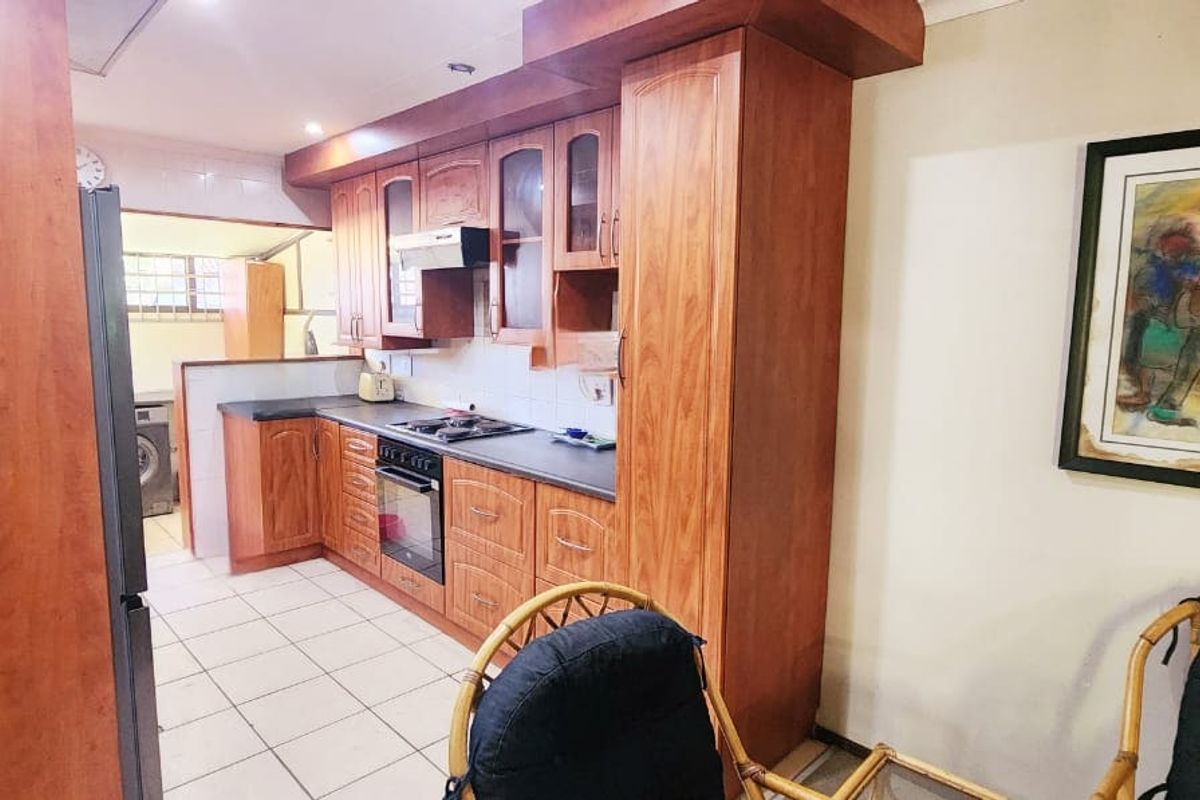 A functional kitchen featuring wood-finish cabinetry, dark laminate countertops, built-in oven and hob, and tiled flooring, with an adjacent laundry area visible.