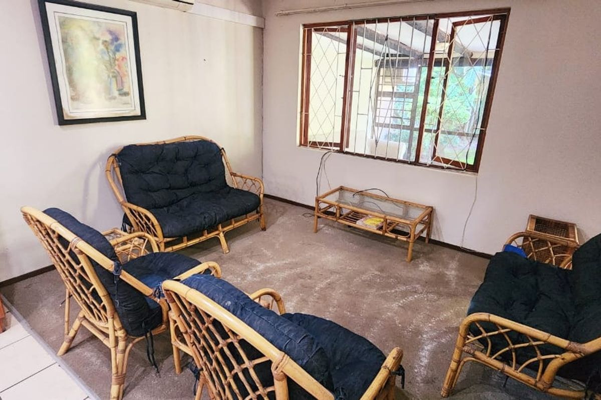 A living room featuring carpet flooring, a built-in cupboard, and window security bars. The space requires cosmetic updates to improve its overall condition.