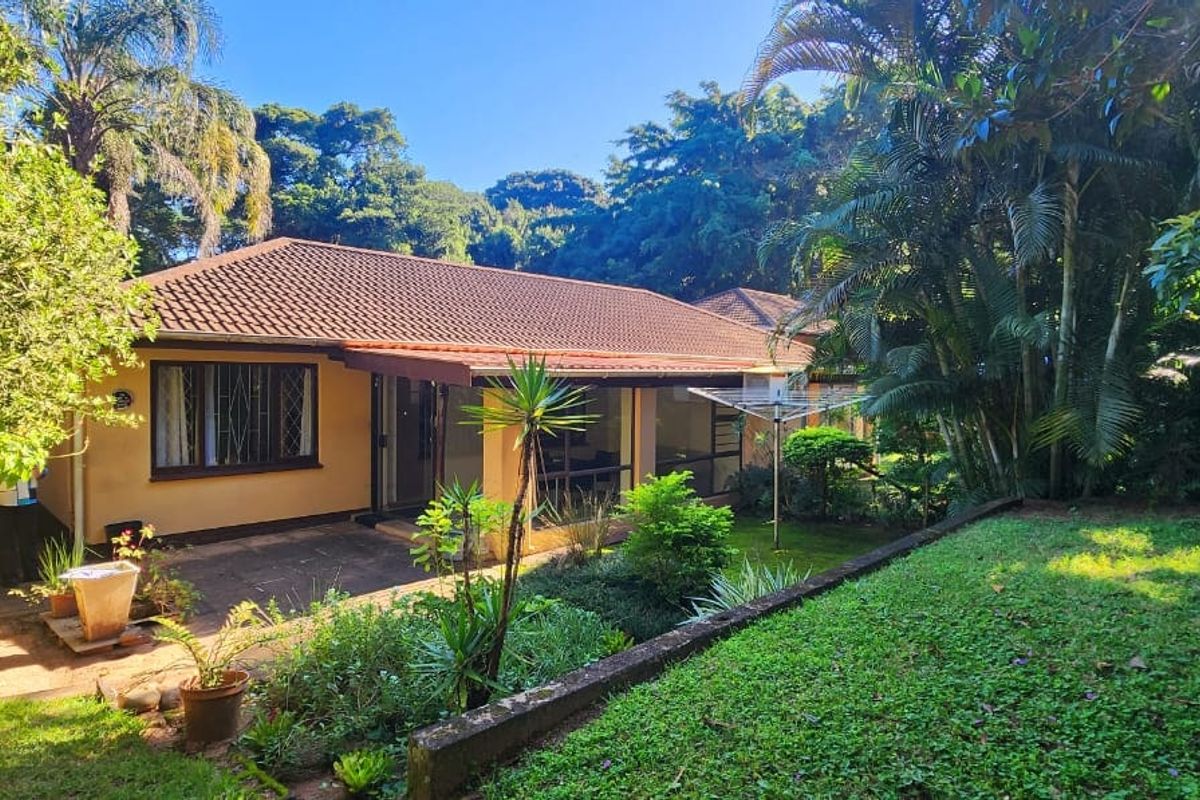 Rear view of the townhouse featuring a paved patio area, tiled roof, and established garden surroundings.