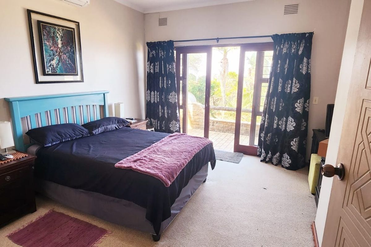 A well-lit bedroom featuring carpeted floors, air conditioning, and direct access to an outdoor patio through glass sliding doors.