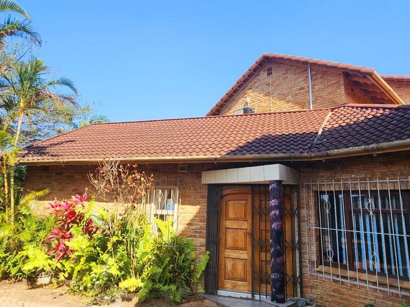 Front elevation of a face brick house featuring a tiled roof, secure entrance with timber door, and established garden surroundings.