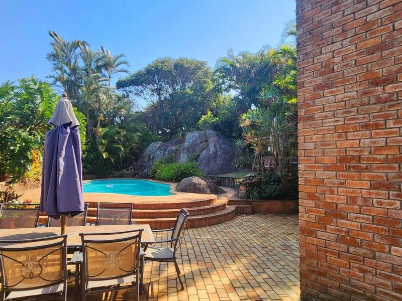 Outdoor entertainment area featuring a swimming pool with a raised deck, surrounded by established garden landscaping and brick paving.