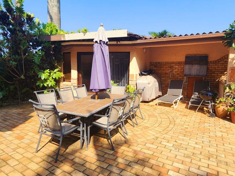 A covered outdoor patio area featuring brick paving and a built-in braai, providing a functional space for outdoor dining and entertainment.