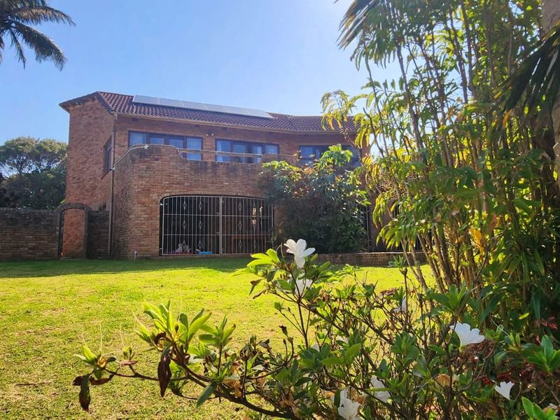 Rear view of a double-story brick house featuring a balcony, solar panels on the roof, and a spacious garden area.