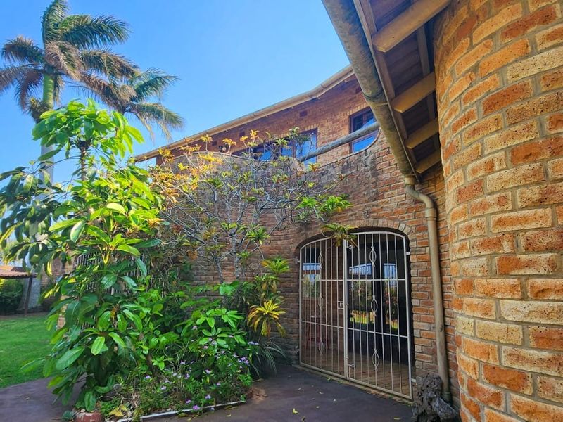 Rear exterior view of a face brick house featuring a paved patio area, security gate, and established garden surroundings.
