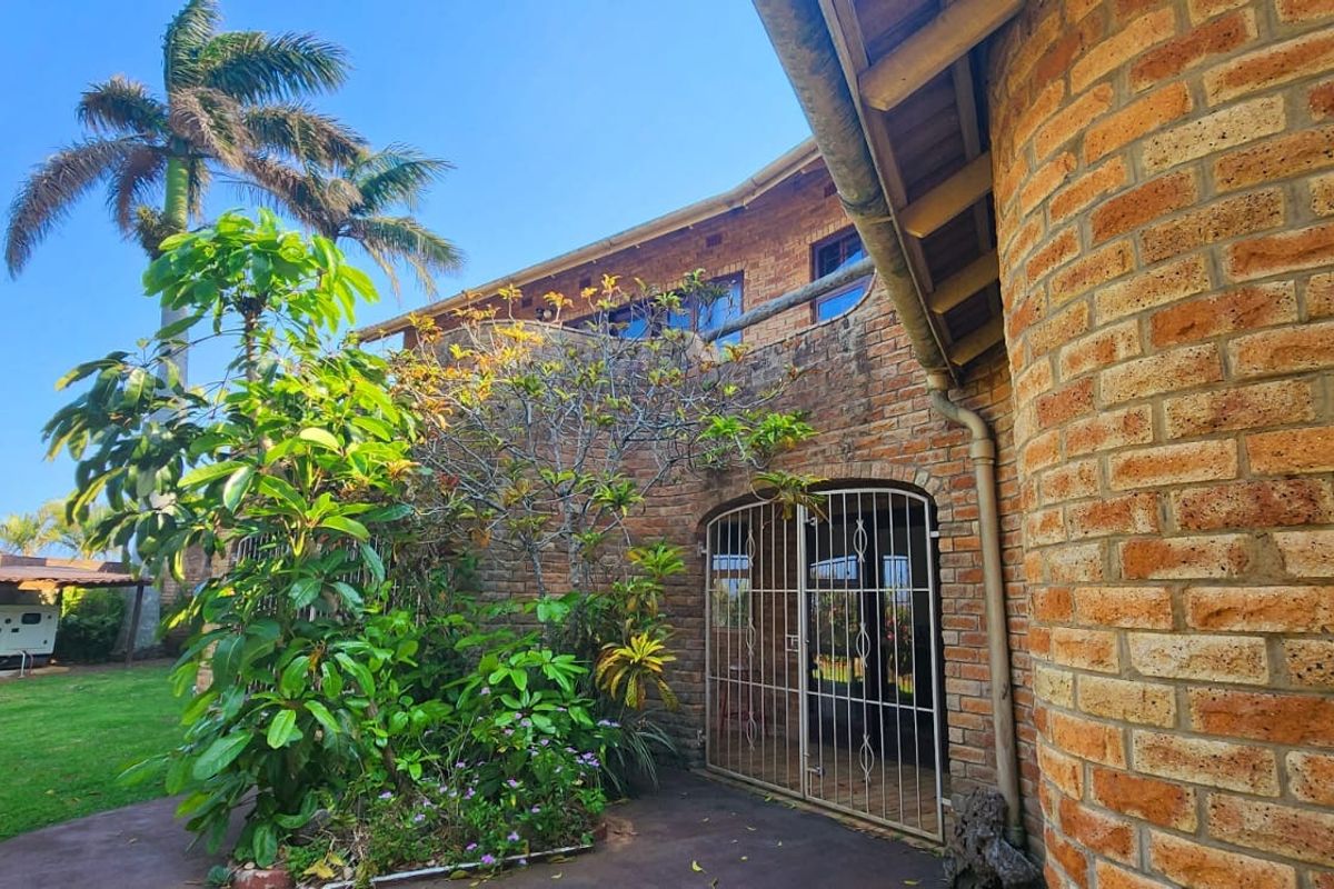 Rear exterior view of a face brick house featuring a paved patio area, security gate, and established garden surroundings.