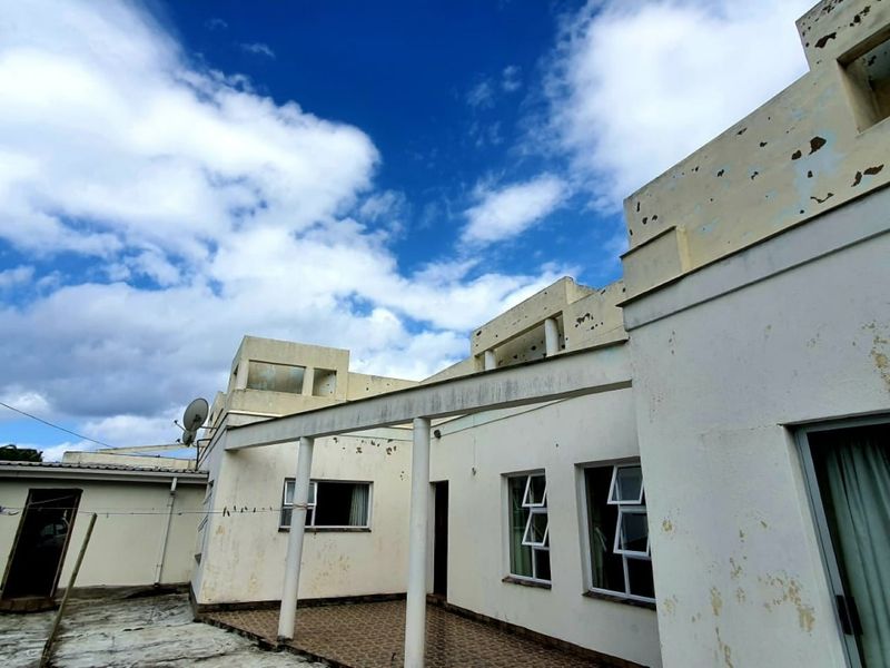 Rear exterior view of the apartment building featuring a covered patio area with tiled flooring and visible signs of exterior paint deterioration.