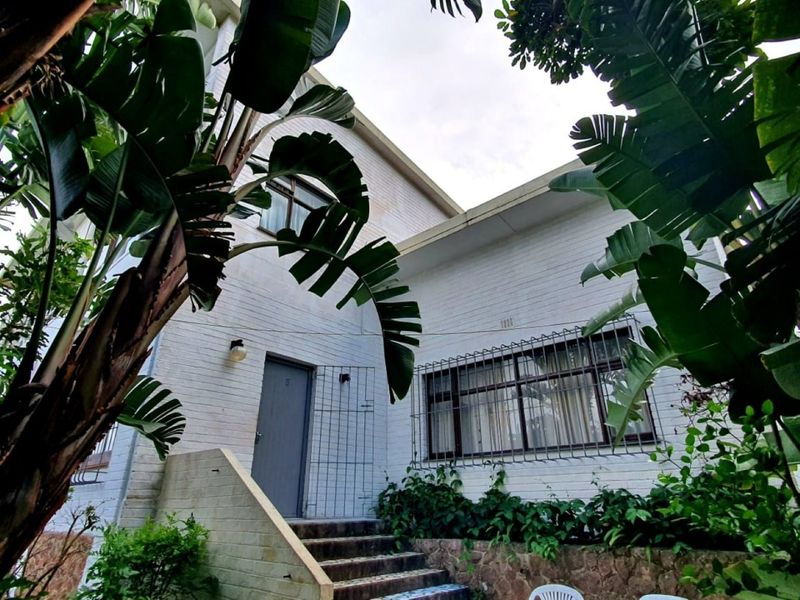 Front entrance view of the apartment building featuring brick facade, security bars on windows, and concrete stairs leading to the front door.