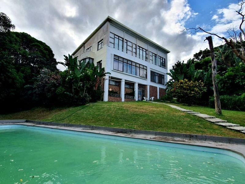 Rear view of a multi-story apartment building featuring balconies and a swimming pool set within a landscaped garden area.