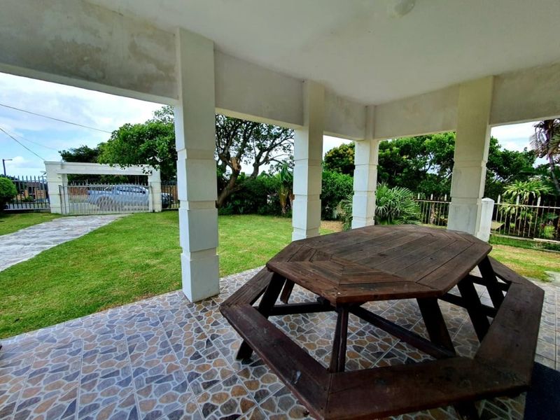 A covered outdoor patio area featuring tiled flooring and concrete support pillars, overlooking a private garden space.