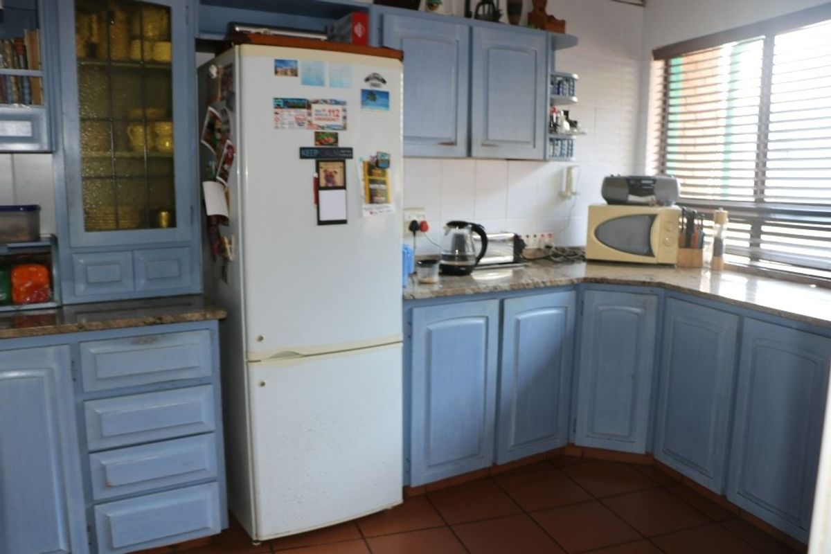 A dated kitchen featuring blue painted cabinetry, granite countertops, and tiled flooring, offering a functional layout with potential for modern renovation.