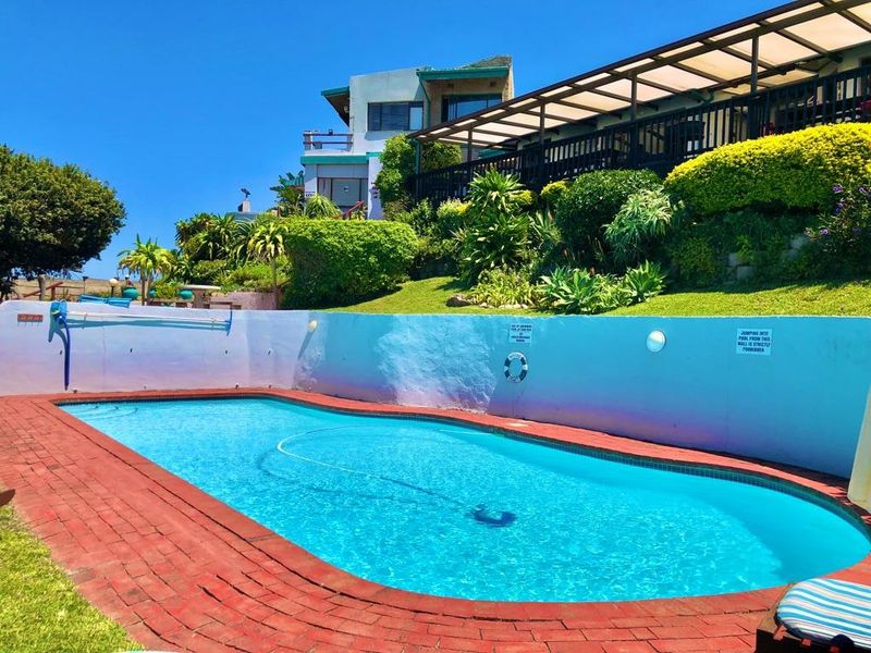 Outdoor swimming pool area featuring brick coping, a retaining wall with garden landscaping, and an elevated covered patio overlooking the pool.