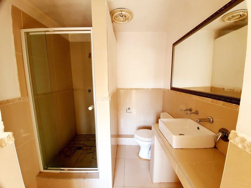 A functional bathroom featuring a tiled vanity with a vessel sink, a glass-enclosed shower, and neutral wall tiling.