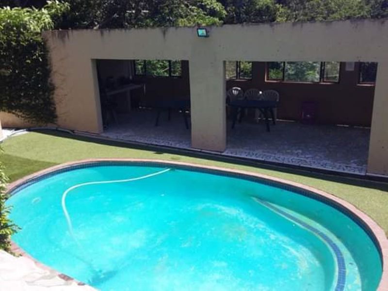 Outdoor entertainment area featuring a swimming pool, artificial lawn, and a covered patio space suitable for relaxation and social gatherings.