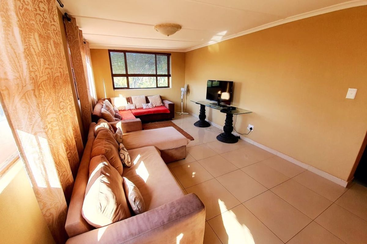 A living room featuring tiled flooring, large windows allowing natural light, and a neutral wall finish.