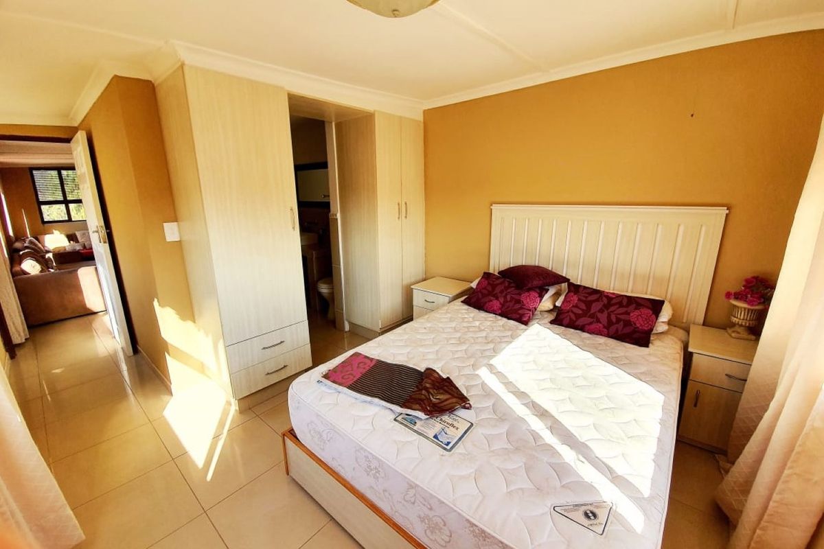 A bedroom featuring built-in cupboards, tiled flooring, and an en-suite bathroom entrance, offering a functional layout with neutral wall tones.