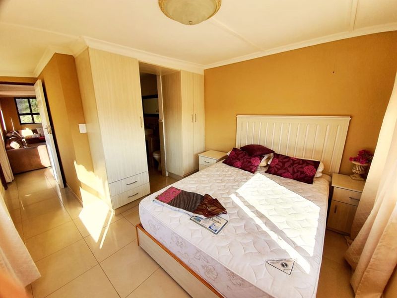 A bedroom featuring built-in cupboards, tiled flooring, and an en-suite bathroom entrance, offering a functional layout with neutral wall tones.