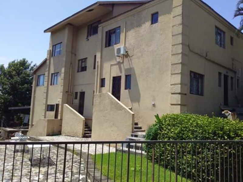 Rear view of a multi-story residential building featuring a stucco facade, external staircases, and a paved patio area.