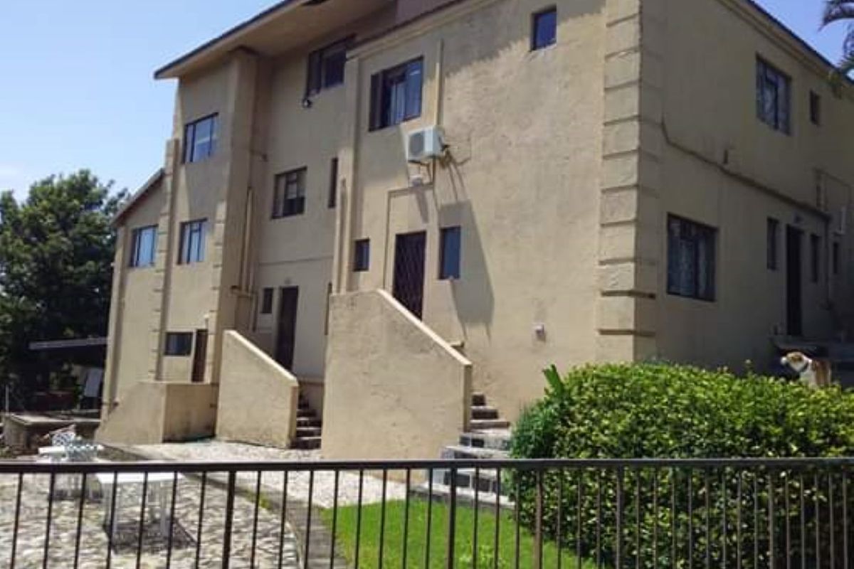 Rear view of a multi-story residential building featuring a stucco facade, external staircases, and a paved patio area.