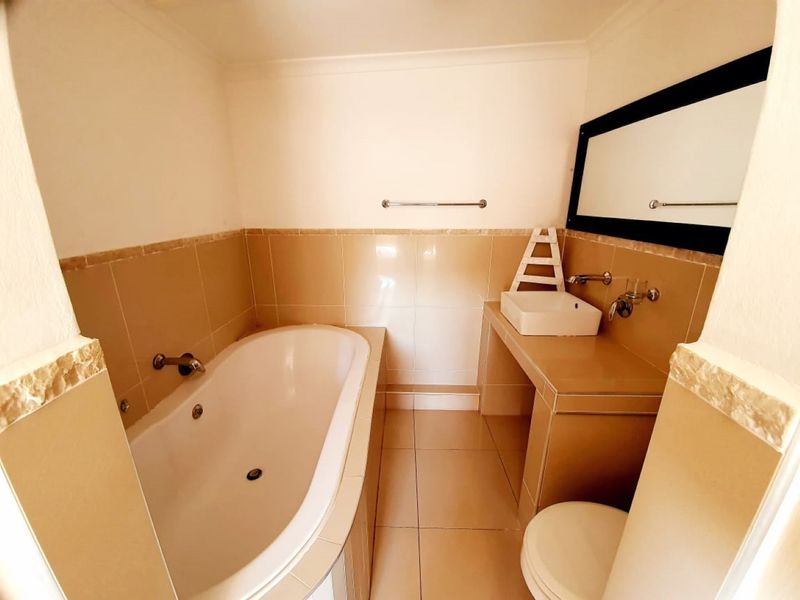 A functional bathroom featuring a built-in bathtub, tiled vanity with a vessel sink, and neutral wall tiling.