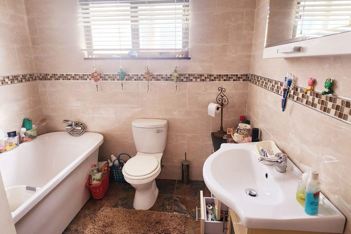 A functional bathroom featuring a bathtub, toilet, and pedestal sink with neutral wall tiling and a decorative mosaic border.