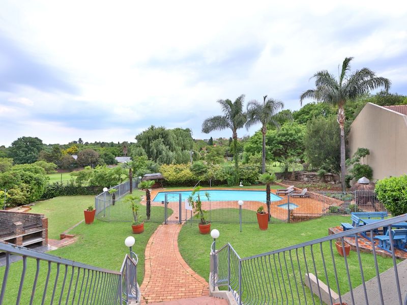 Outdoor pool area featuring a swimming pool, brick paved pathways, built-in brick braai, and metal fencing set within a landscaped garden.