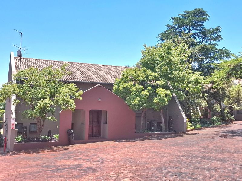 Front exterior view of the apartment building featuring a tiled roof, covered entrance, and a brick-paved driveway surrounded by mature trees.