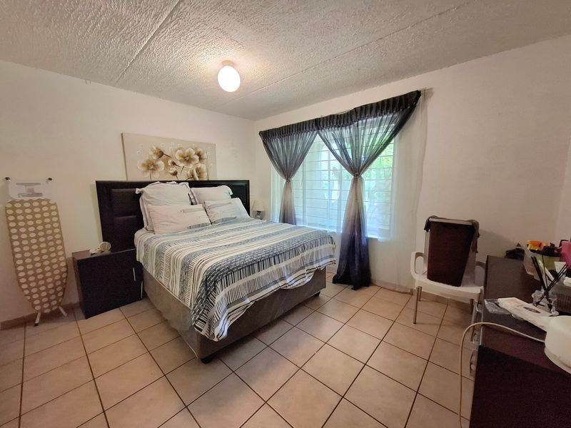 A bedroom featuring tiled flooring, a textured ceiling, and a window fitted with security bars.
