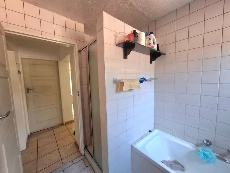 Bathroom featuring a built-in bathtub and separate shower enclosure with white ceramic tiling throughout. Requires cosmetic updates to finishes and grout.