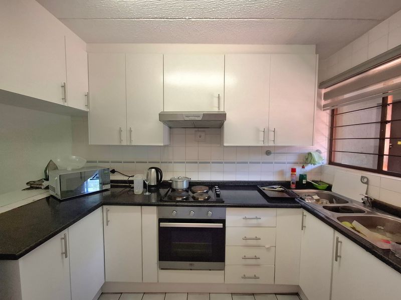 A functional kitchen featuring white cabinetry, dark granite countertops, a built-in oven, electric hob, and a double bowl sink with tiled backsplash.