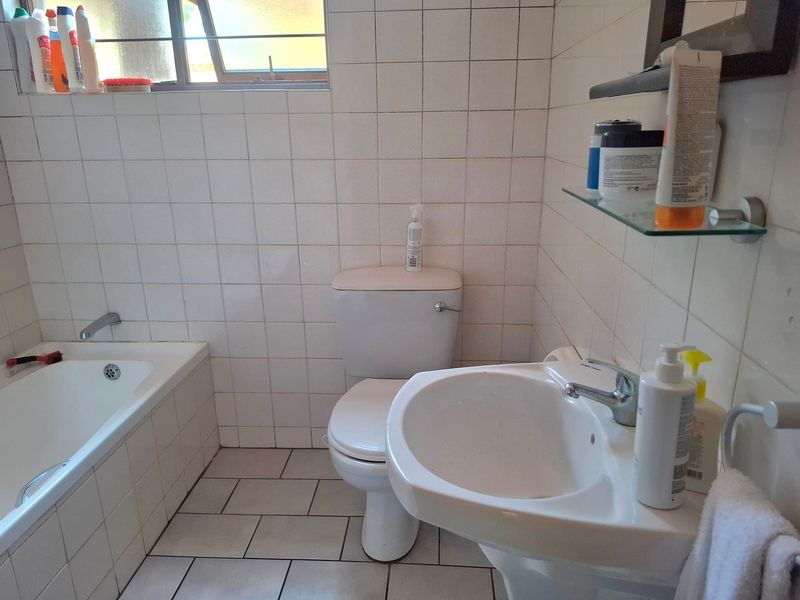 A functional bathroom featuring a bathtub, pedestal basin, and toilet with white ceramic wall and floor tiling.