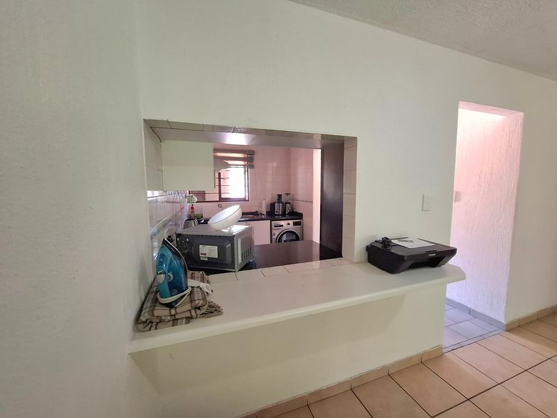 A functional kitchen featuring a breakfast bar pass-through, tiled flooring, and cabinetry, offering a practical layout with potential for modern cosmetic updates.