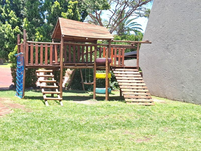 A communal garden area featuring a wooden jungle gym structure set on a well-maintained lawn.