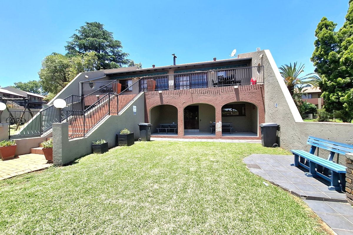 Rear view of the apartment building featuring a covered ground-floor patio, an upper-level balcony with metal railings, and a private lawn area.