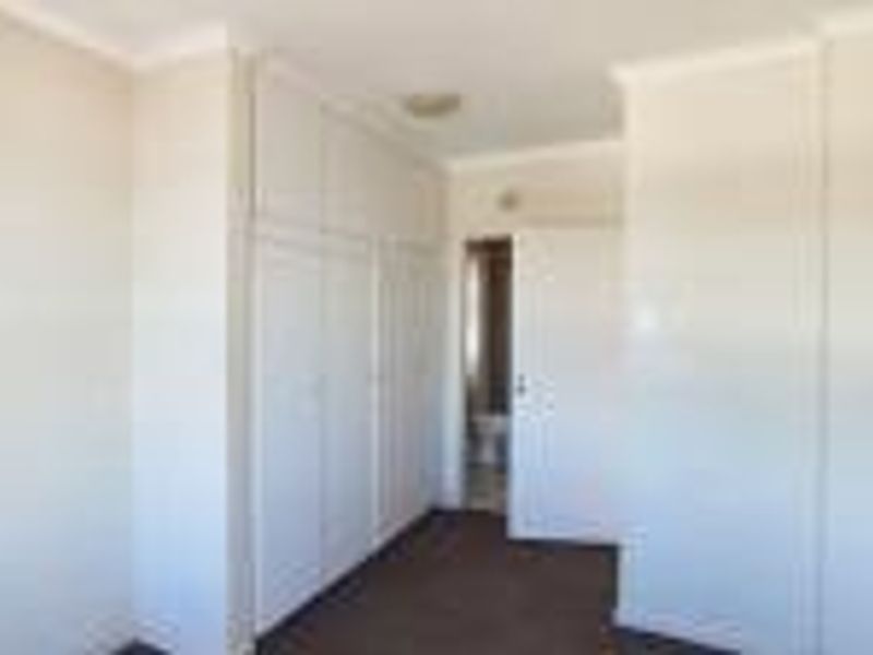 A clean, empty bedroom featuring built-in cupboards, neutral wall finishes, and carpeted flooring, offering a blank canvas for personalization.