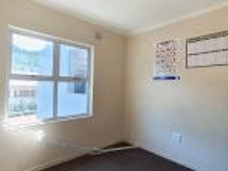 A vacant bedroom featuring neutral walls, carpeted flooring, and an aluminium-framed window, offering a blank canvas for personalization.