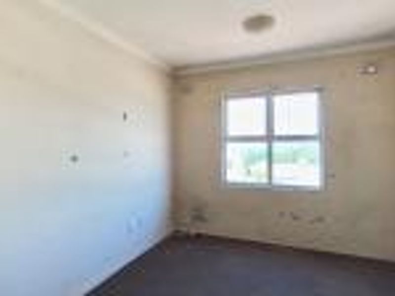 An empty bedroom featuring carpet flooring and a window, currently requiring wall repairs and repainting to restore its condition.