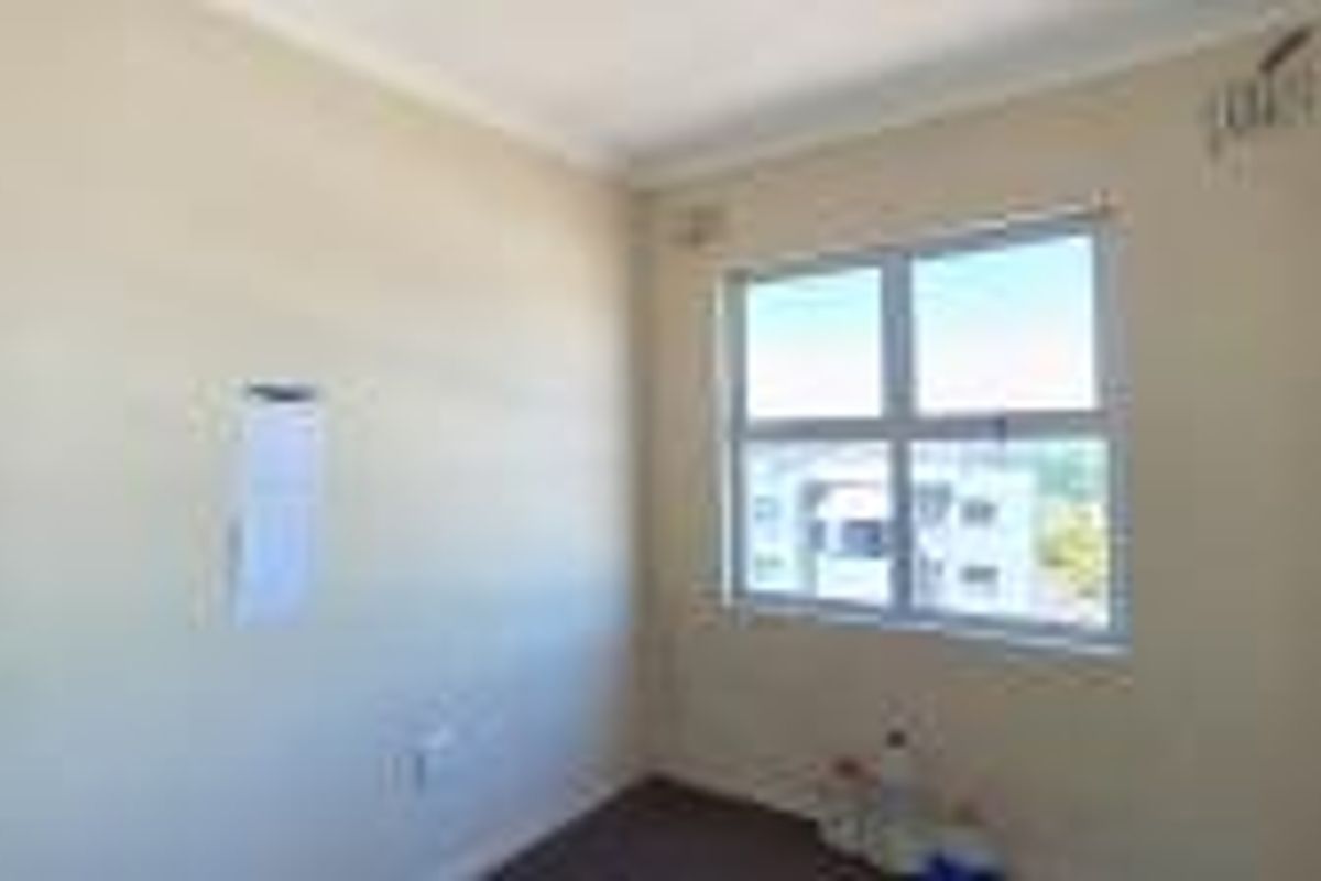 An empty bedroom featuring neutral walls, cove cornicing, and an aluminium-framed window with natural light.