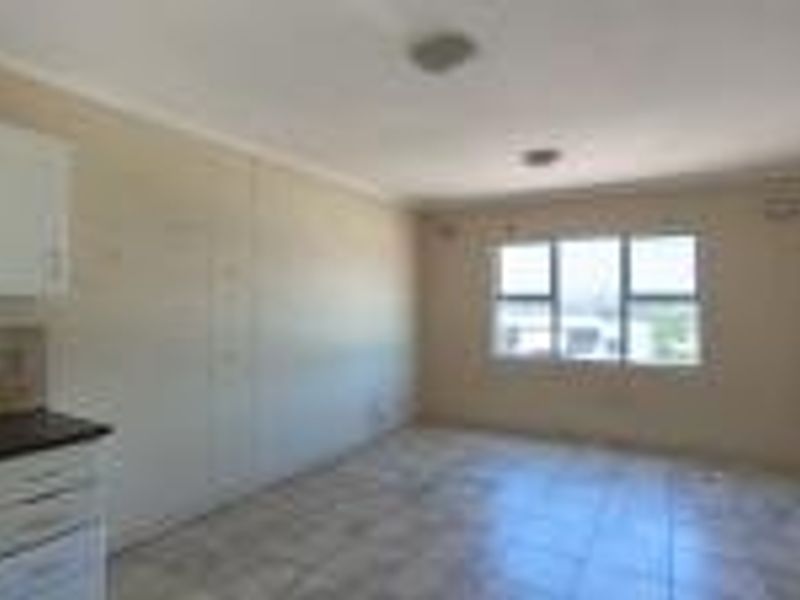 An empty open-plan living and kitchen area featuring tiled flooring, built-in cabinetry, and a built-in oven, offering a blank canvas for renovation.