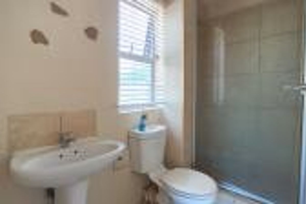 A functional bathroom featuring a pedestal basin, toilet, and a glass-enclosed shower with tiled walls.